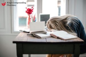 Woman resting her head on a desk surrounded by books