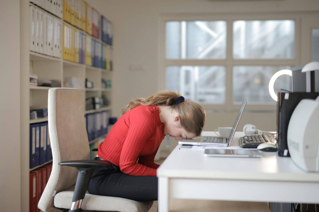 Woman sitting at a desk with her head down, feeling exhausted